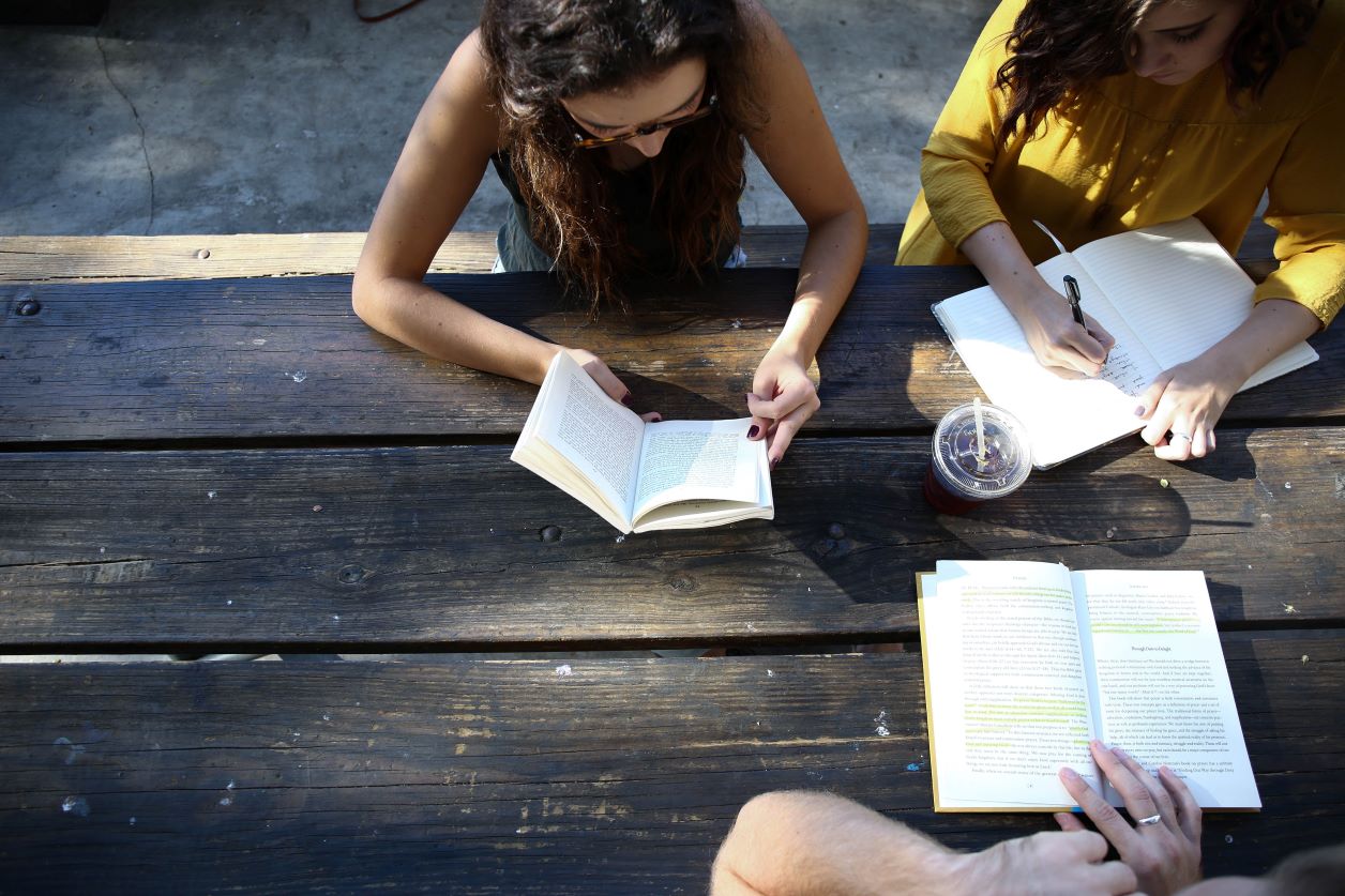 three people sitting in a park reading and taking notes