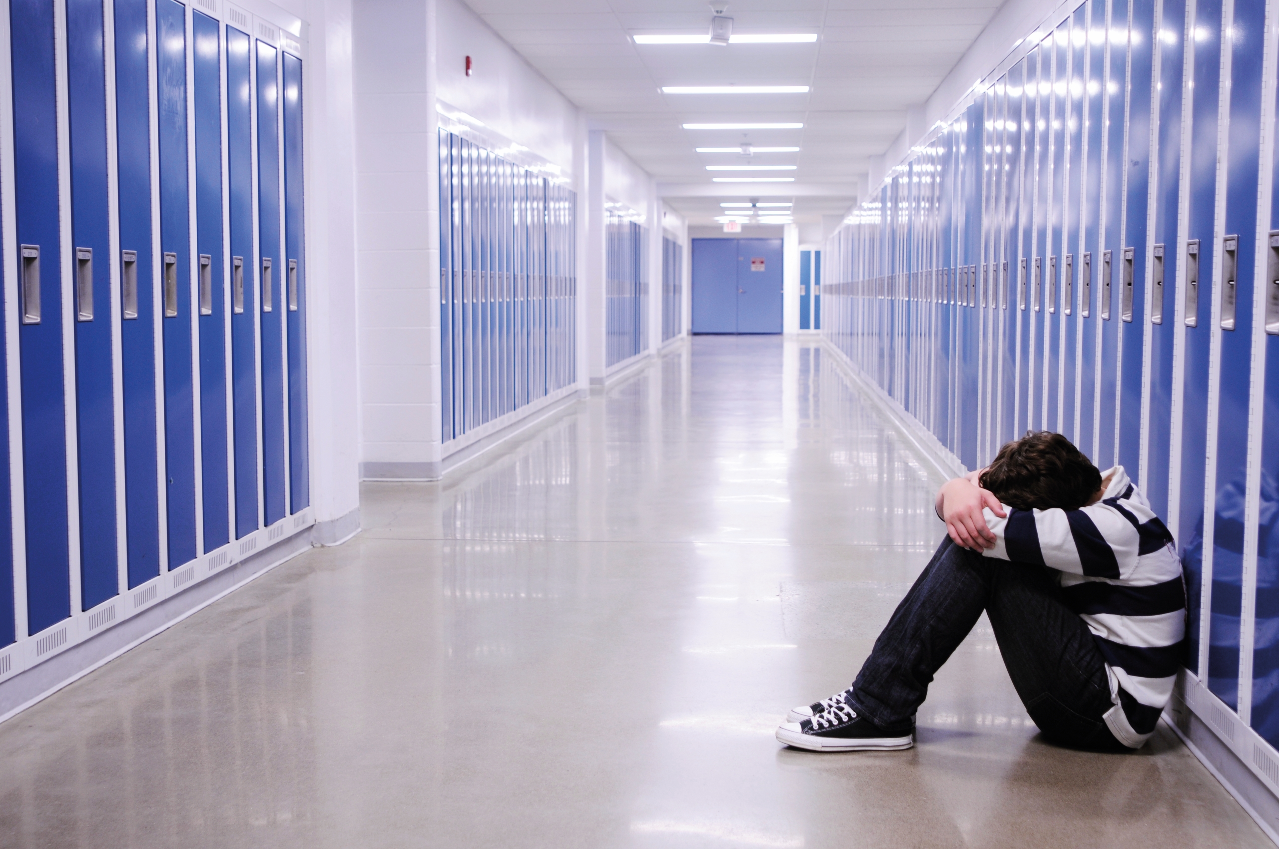 picture of a school hallway with a someone curled up sitting against the locker